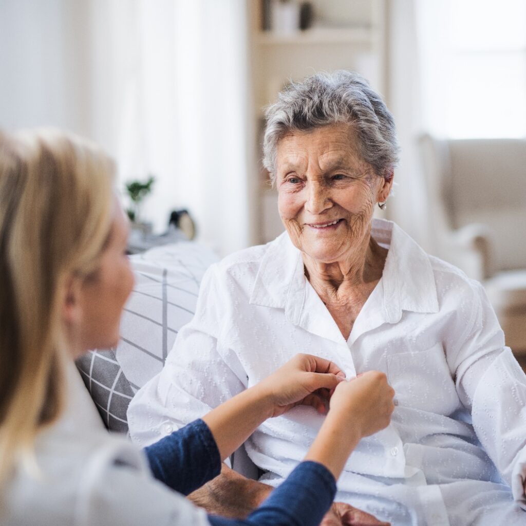 A health visitor helping a sick senior woman sitting on bed at home.