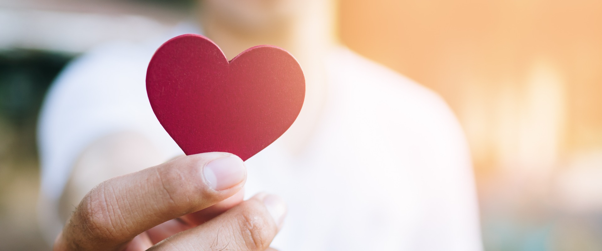 Asian man hold red heart shaped wooden piece with blur background